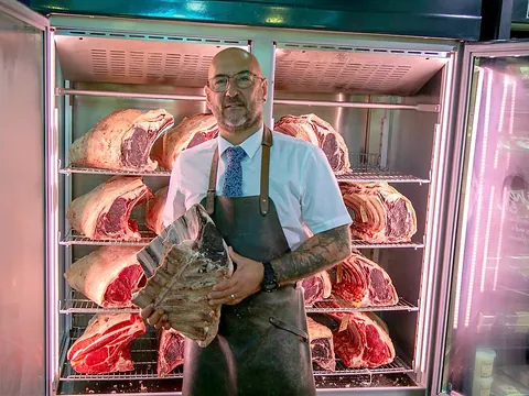 A Newlyns butcher in front of the dry-ageing cabinet full of beef