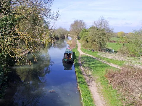 The Basingstoke Canal near Odiham, with a narrowboat moored by the towpath under a blue sky